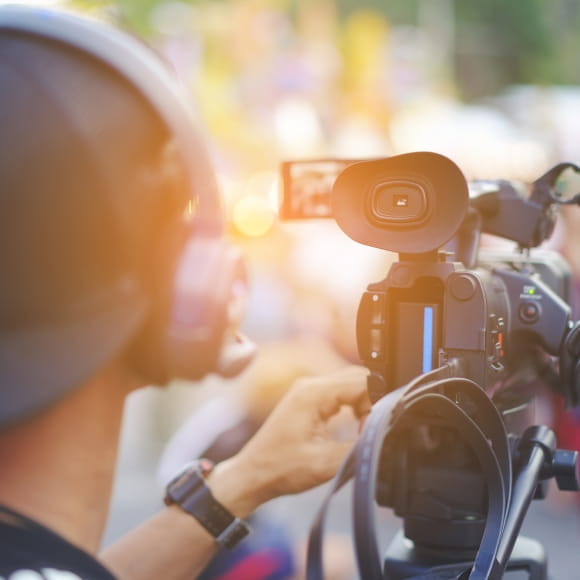Eine Reporterin hält ein Mikrofon in Richtung der Kamera und lächelt.